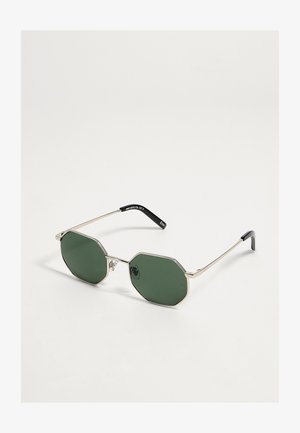 Lunettes de soleil octogonales avec fines montures en métal doré et verres vert foncé sur fond blanc.