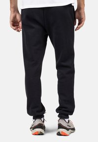 Sorte sweatpants lavet af blødt stof, med elastisk talje, sidelommer og tætsiddende ben. Båret med sneakers.