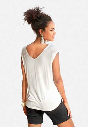 White, lightweight short-sleeve top with a V-neckline and relaxed fit, paired with dark shorts. Notable texture appears soft and smooth.