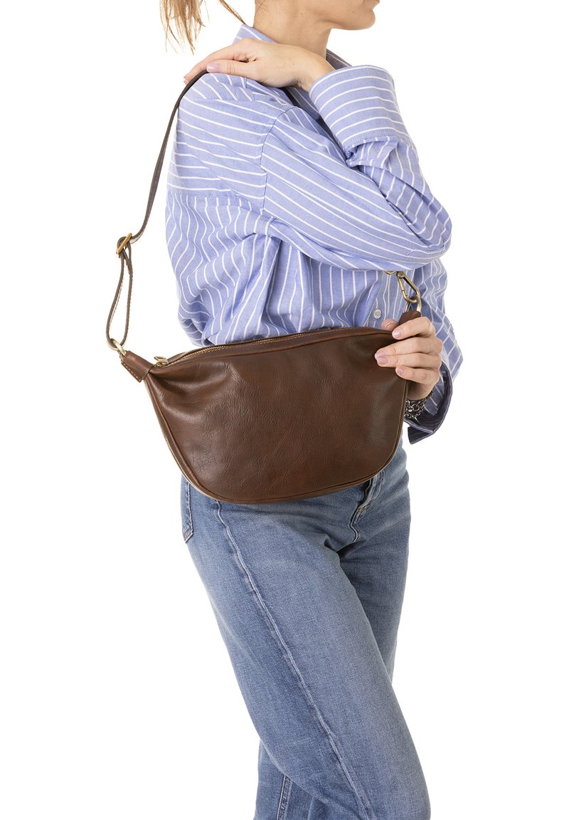 Borsa a spalla in pelle marrone con forma curvata, tracolla regolabile, chiusura a zip e texture liscia. Indossata sopra una camicia a righe blu.