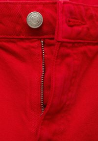 Rode spijkerbroek van denim met een zilveren knoopsluiting, een metalen rits en versterkte stitching langs de tailleband en de gulp.