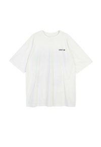 Biała, oversize'owa koszulka z miękkiego materiału, z okrągłym dekoltem i krótkimi rękawami. Napisy "LUCKY ME" w kolorze czarnym znajdują się po lewej stronie.