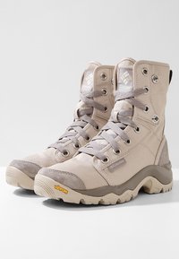 Béžové šněrovací boty s vysokým designem, které mají svršek z plátna a semiše, kovové očka a podrážku Vibram pro přilnavost.