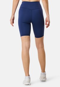 Shorts bike blu navy a vita alta con cintura senza cuciture e una texture liscia e elastica, abbinati a scarpe da ginnastica bianche.