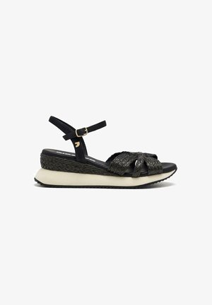 Sandal con cinturino intrecciato nero, soletta in gomma, cinturino alla caviglia regolabile e una piattaforma imbottita con accenti bianchi a contrasto.