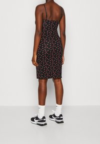 Schwarzes, eng anliegendes Kleid mit dünnen Trägern, versehen mit einem Kirschmuster. Kombiniert mit schwarz-weißen Nike-Sportschuhen und weißen Socken.