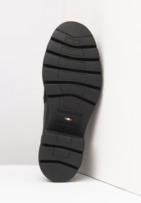 Suola di scarpa in gomma nera con motivo di battistrada testurizzato, con marchio in rilievo. Finitura liscia e etichetta "made in Italy" visibile.