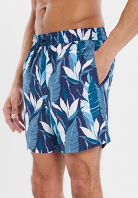 Costumi da bagno con un motivo di foglie tropicali blu e teal, cintura elastica e tasche laterali. Realizzati in materiale leggero e a asciugatura rapida.