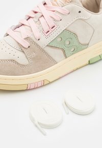 Sneakers in suede di colore beige, verde e rosa. Caratteristiche includono lacci rosa, una suola in gomma colorata e due lacci bianchi aggiuntivi.