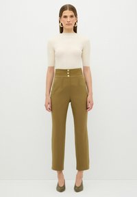 Beige přiléhavý top v kombinaci s olivově zelenými kalhotami s vysokým pasem, které mají tři dekorativní knoflíky a rovný střih. Hladká textura látky.