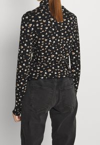 Schwarzes Langarmoberteil mit einem floralen Muster in Weiß und Braun. Figurbetontes Design mit geripptem Textur und hochgeschlossenem Kragen.