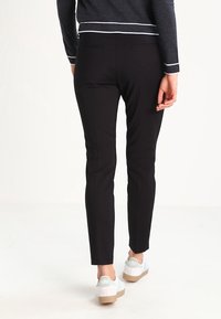 Pantalon noir à coupe slim, en tissu lisse, avec poches arrière, associé à des baskets blanches et un haut bleu marine.
