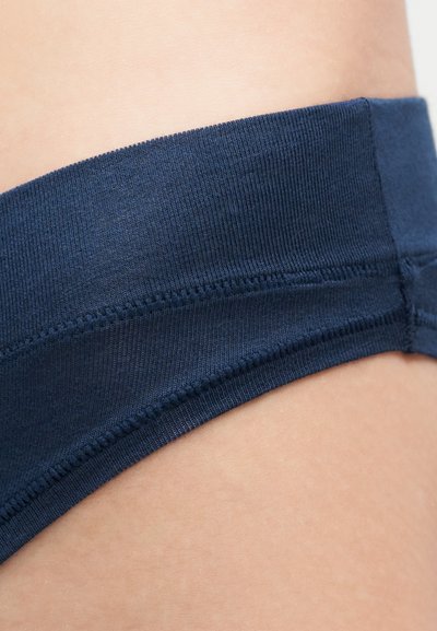 Κοντινό πλάνο στη μέση ενός ατόμου που φοράει εσώρουχο από σκούρο μπλε ριμπ ύφασμα με εμφανείς ραφές και δέρμα ορατό πάνω και κάτω από τη ζώνη της μέσης.