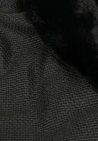 Tessuto verde scuro con una trama strutturata e un motivo tessuto, bordato da un morbido trim in pelliccia sintetica nera lungo il margine.
