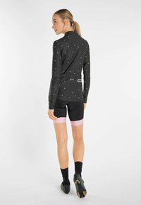 Black long-sleeve cycling jersey with reflective dots, paired with black shorts featuring a pink accent. Close-fitting design and textured fabric.