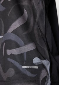Sort aktivtøjstop med abstrakte grå mønstre. Har ACTIBREEZE branding og et glat, tekstureret stof, der giver åndbarhed.