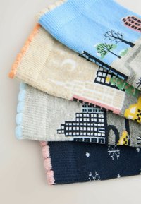 M�önstrade strumpor i blått, beige, grått och marinblått med texturerade kanter. Mönstren inkluderar träd, byggnader och säsongsbetonade motiv. Mjukt stickat tyg.