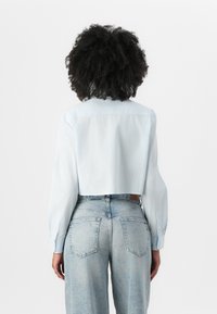 Light blue cropped shirt made of fabric with a subtle texture, featuring long sleeves and buttoned cuffs, paired with high-waisted denim jeans.
