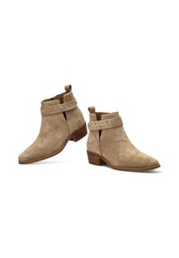 Botas de tobillo de ante en beige con punta afilada, cortes laterales y una correa con tachuelas alrededor del tobillo. Tacón bajo apilado.