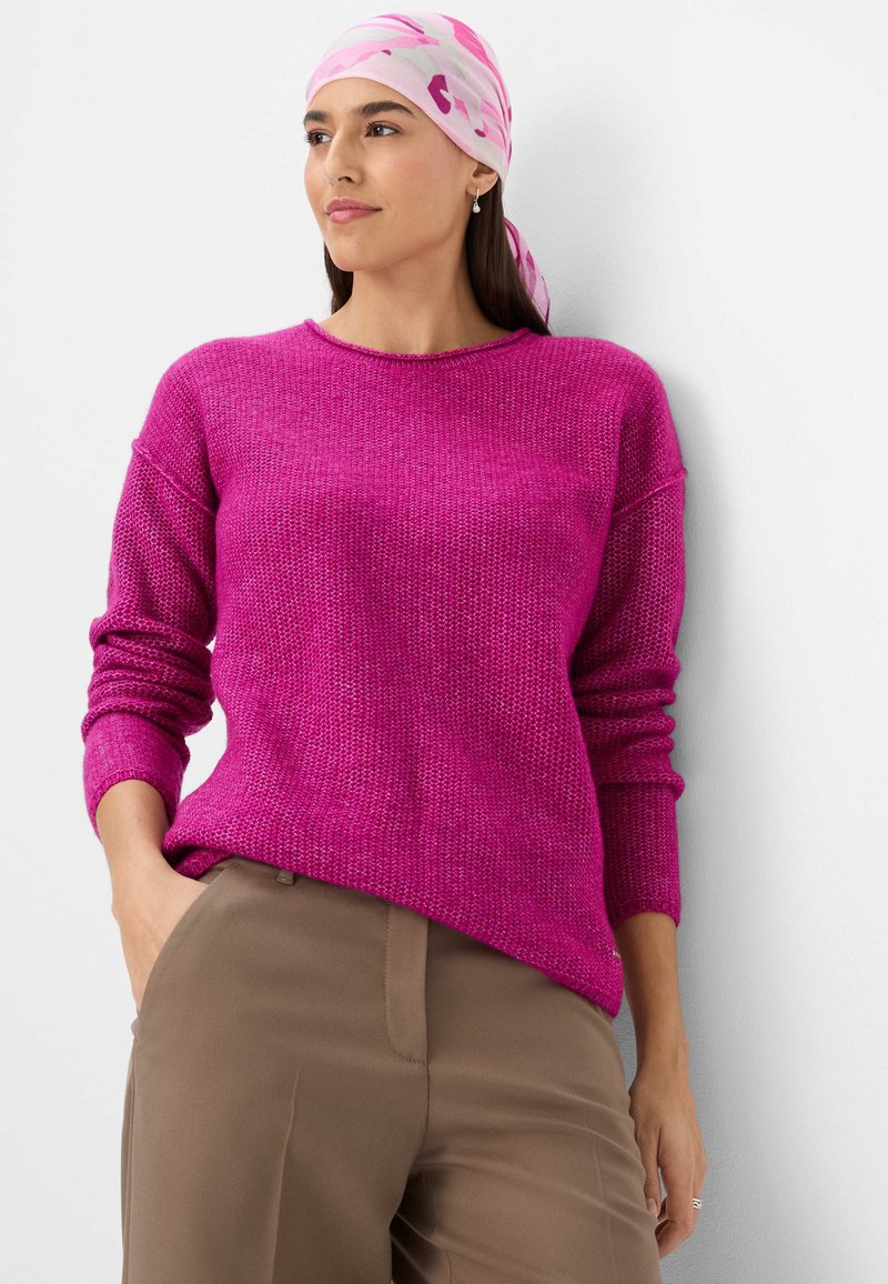 Fuchsia Strickpullover mit strukturiertem Stoff, Rundhalsausschnitt und überschnittenen Schultern, kombiniert mit beigen Hosen. Dazu ein gemusterter rosafarbener Schal.