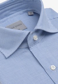 Lyseblå ternet skjorte lavet af bomuld, med spidse kraver, hvide knapper og et mærke syet indeni kraven.