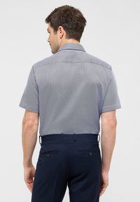 Camicia a maniche corte con un motivo geometrico blu navy e bianco, design con colletto e una texture del tessuto liscia. Abbinata a pantaloni blu navy scuri.