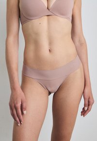 Beha en slipset in zachte, rekbare beige stof. De beha heeft gladde cups met subtiele stiksels; de slip heeft een brede tailleband en biedt minimale bedekking.