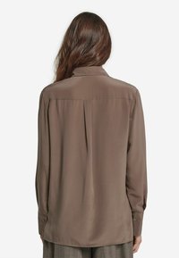 Brun, långärmad skjorta i slät tyg. Har en krage och en centralt ryggveck. Klädda manschetter med matchande knappar.