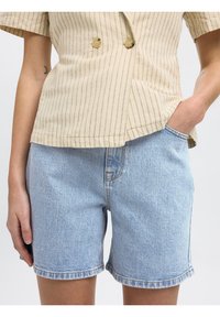 Haut à boutons beige à rayures avec des manches courtes, associé à un short en denim bleu clair à coupe classique et avec des détails de couture visibles.