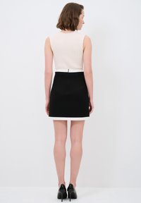 Top beige tanpa lengan bertekstur dirib dengan rok mini hitam yang memiliki garis tepi putih. Rok tersebut dilengkapi dengan detail ritsleting di bagian belakang. Sepatu hak hitam melengkapinya.