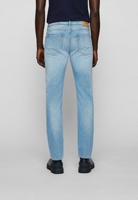 Jean bleu clair en denim, présentant une coupe droite, deux poches arrière et une étiquette en cuir marron clair à la ceinture.