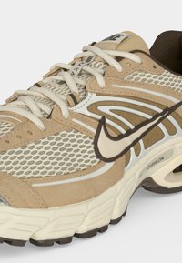 Chaussure de running Nike Air Max beige et crème avec panneaux en mesh, lacets blancs, doublure intérieure marron et semelle amortie avec unité d’air visible.