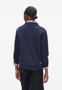 Marinblå sweatshirt med ribbad krage, långa ärmar och randiga muddar. Har en logotyp vid nederkanten och en avslappnad passform.