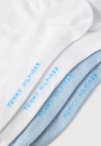 Τέσσερα διπλωμένα κάλτσες αστραγάλου σε λευκό και ανοιχτό μπλε, κάθε μία με την επιγραφή "TOMMY HILFIGER" σε ανοιχτό μπλε χρώμα κατά μήκος της σόλας.