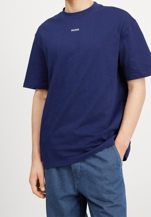 Granatowa bawełniana koszulka z krótkim rękawem i okrągłym dekoltem. Posiada białe logo "HUGO" na piersi. Miękka tekstura, luźny krój.