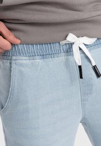 Jasnoniebieskie dżinsowe joggery z elastycznym pasem i białym sznurkiem. Posiadają boczne kieszenie i subtelną teksturę.