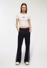 Biała krótka koszulka z nadrukiem "BROOKLYN NYC" w kolorze czarnym. Granatowe spodnie z bocznymi białymi paskami, luźny krój, elastyczny pas i kieszenie.