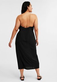 Schwarzes Satin-Midikleid mit dünnen Kettenträgern, rückenfreiem Design und fließender Textur. Knielange Länge mit geradem Saum.