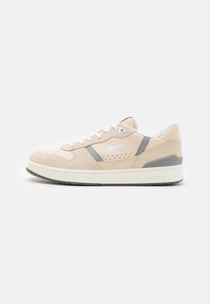 Baskets basses beige et grises avec semelle blanche et lacets, panneaux latéraux perforés, et logo crocodile sur le côté.