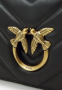 Borsa a mano in pelle nera con trapuntatura a zigzag, decorata con un anello dorato e due motivi di uccelli finemente dettagliati. Marca "PINKO."