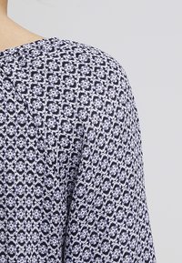 Tissu à motifs avec un design floral bleu et blanc sur un fond sombre ; texture lisse ; vêtement léger et ample.