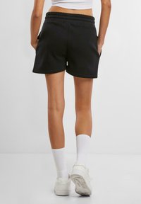 Schwarze Baumwollshorts mit elastischem Bund und Seitentaschen. Kombiniert mit weißen kniehohen Socken und weißen Turnschuhen. Einfaches, lässiges Design.