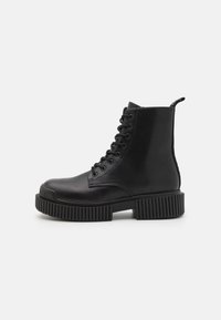 Mustat nauhaketjut ankle-bootsit, jotka on valmistettu sileästä nahasta. Niissä on paksu uritettu pohja ja vahvistettu kantapää. Takana on vetoketju helppoa pukemista varten.
