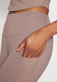Light brown activewear leggings with a high waistband, side pocket, and flat seams for comfort. Smooth texture with a fitted design.