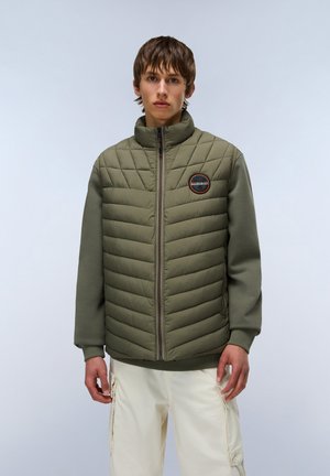 Olive green padded jacket with a high collar and quilted design. Features a zip closure, ribbed cuffs, and a circular patch on the chest.