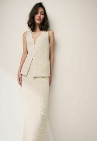 Ensemble tricoté à deux pièces en blanc cassé, comprenant un haut sans manches avec un décolleté en V profond et une longue jupe ajustée en tissu texturé.