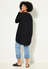 Maglione nero a maniche lunghe con una vestibilità rilassata, caratterizzato da un orlo arrotondato. Abbinato a jeans cropped chiari e strappati, e scarpe black slip-on.