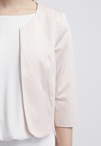 Lichtroze cropped jack met driekwartmouwen, glad satijnstof, ronde halslijn en subtiele naden aan de voorkant.