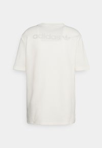 Valkoinen lyhythihainen vohvelikuvioinen t-paita, jossa on Adidas-logo ja kolmonen-symboli painettuna hienovaraisesti valkoisena yläselkään.