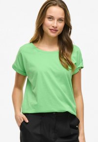 Grön bomulls t-shirt med rund halsringning och korta uppvikta ärmar, kombinerad med svarta byxor. Avslappnad passform och mjuk textur.